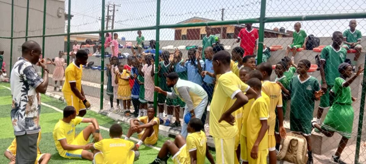 Adetola students and coach by the sports pitch fence